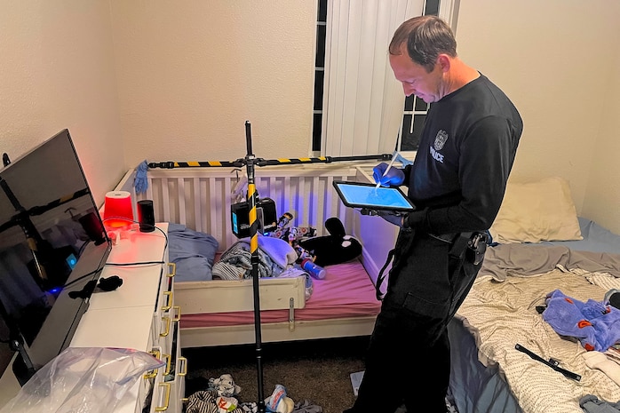 Person standing in a messy bedroom typing something on an iPad