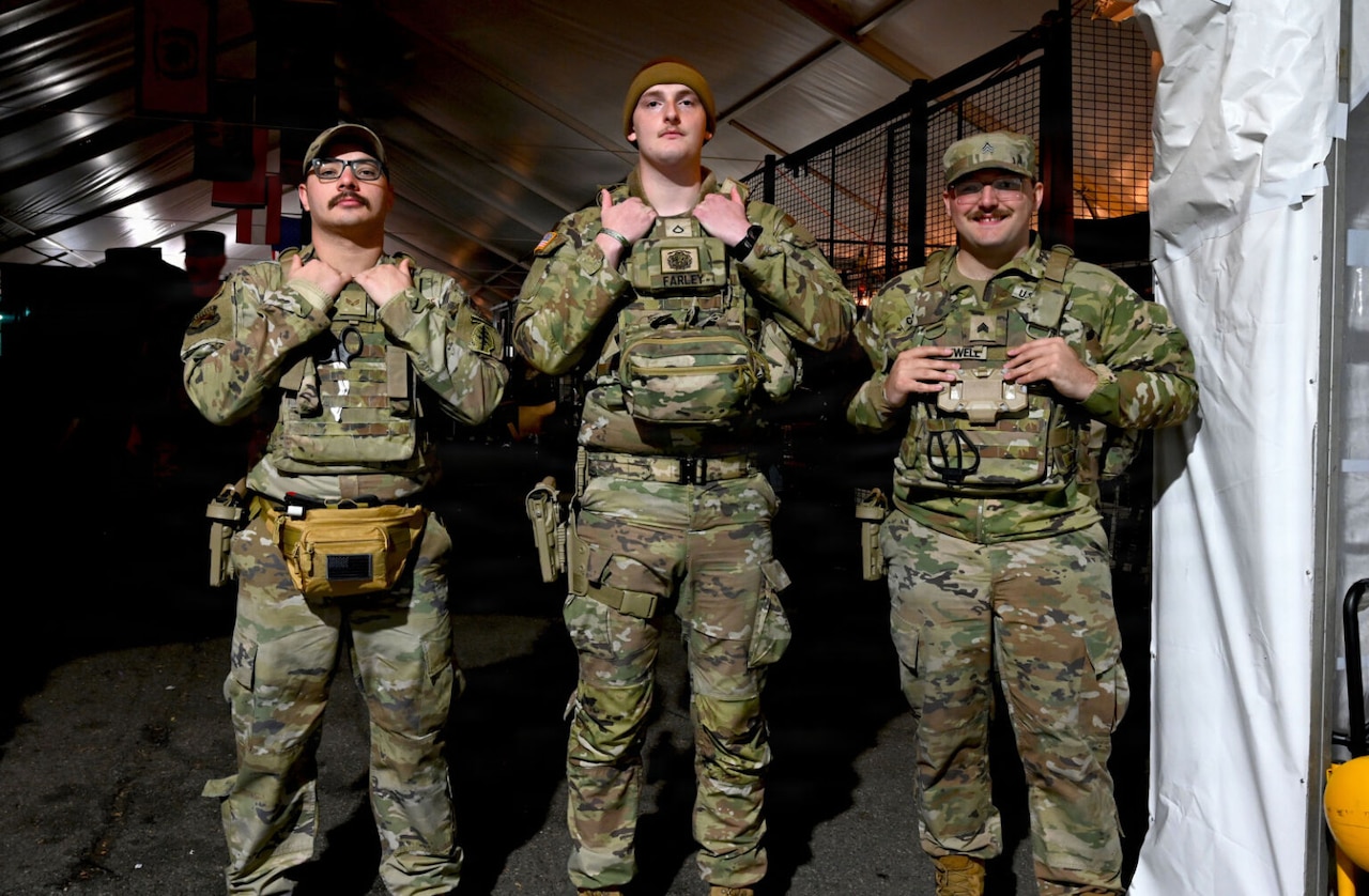 Three men wearing military camouflage uniforms pose for a photograph.