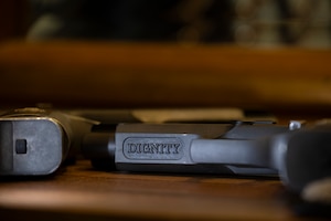 Image of the underside of a dark pistol that has the word DIGNITY inscribed on the barrel.