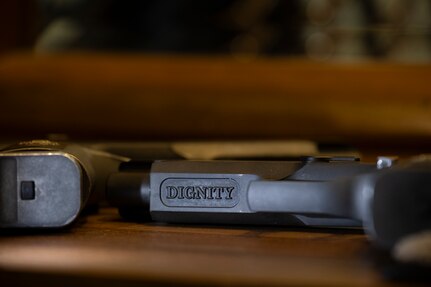 Image of the underside of a dark pistol that has the word DIGNITY inscribed on the barrel.