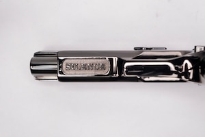 Image of the underside of the barrel of a shiny pistol with the word SILENCE inscribed on it.