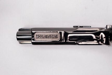 Image of the underside of the barrel of a shiny pistol with the word SILENCE inscribed on it.