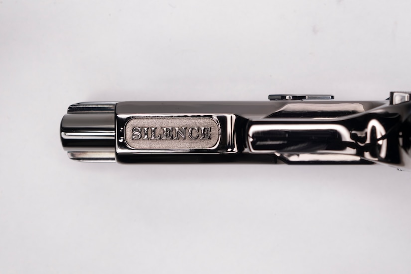 Image of the underside of the barrel of a shiny pistol with the word SILENCE inscribed on it.
