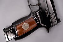 Image of a shiny pistol with wood on the stock, the word PEACE on the end of the magazine, and the letters XXI inscribed on it near the hammer.