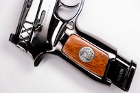 Image of a shiny pistol with wood on the stock and the letters XXI inscribed on it near the hammer.