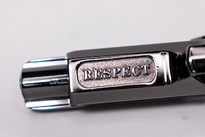 Close-up shot of the silver barrel of a pistol that has the word RESPECT inscribed on it.