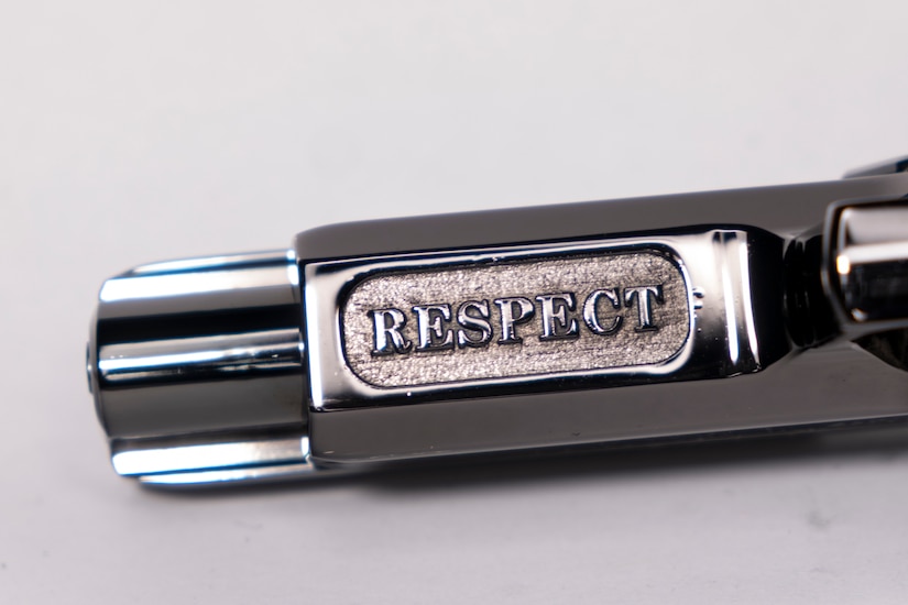 Close-up shot of the silver barrel of a pistol that has the word RESPECT inscribed on it.