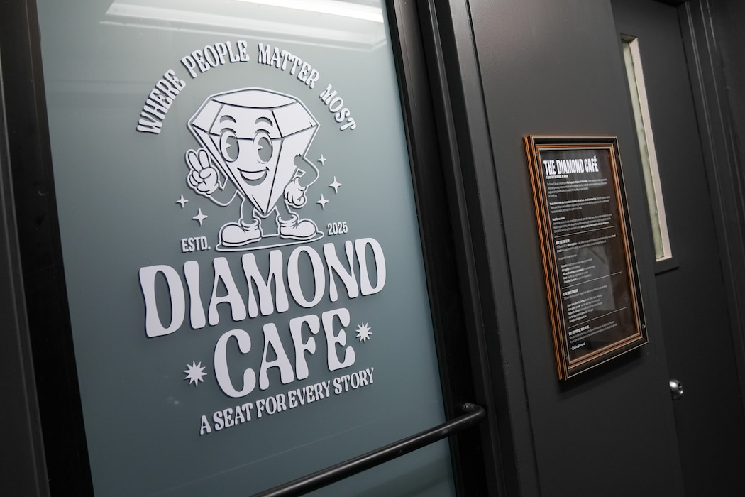 a white sign on a glass door features a diamond shaped character and says Diamond Cafe, a seat for every story