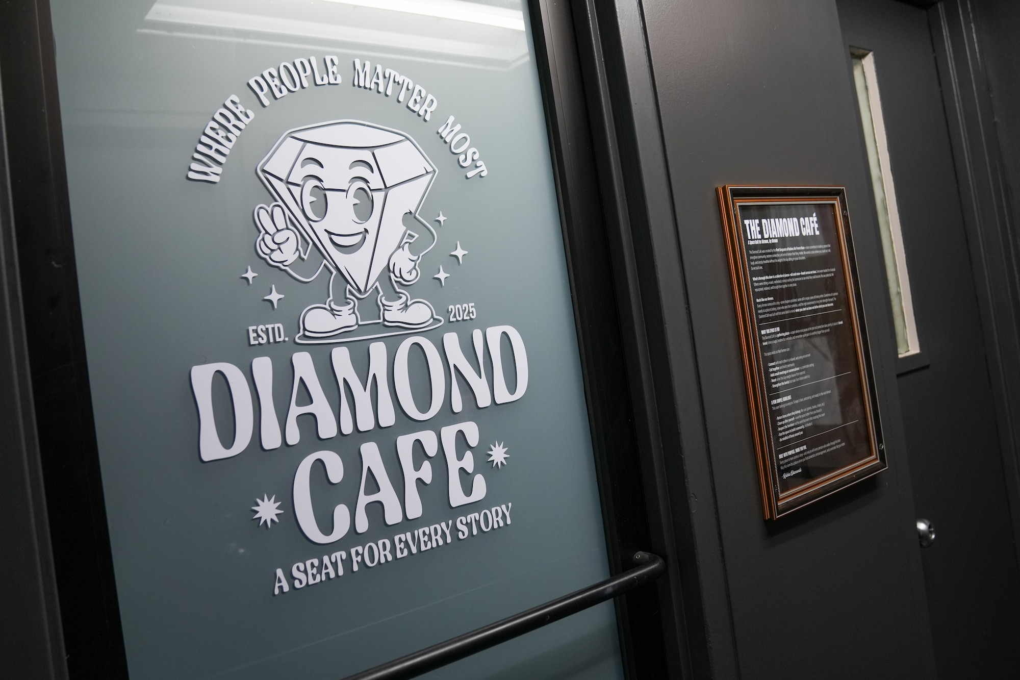 a white sign on a glass door features a diamond shaped character and says Diamond Cafe, a seat for every story
