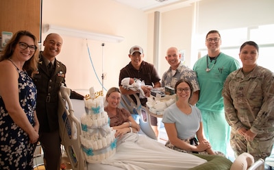 Staff from the Mother Baby Unit at Tripler Army Medical Center, along with Col. William Bimson, commander of TAMC, presented a baby gift basket to U.S. Army Capt. Henry Zenger and Capt. Cecilia Zenger after the birth of their son, Gus Zenger, at TAMC in Honolulu, Hawaii, on Jan. 1, 2026. Gus, born at 5:16 a.m. on New Year’s Day, is TAMC’s first baby boy of 2026. (Defense Health Agency photo by Khinna Kaminske)