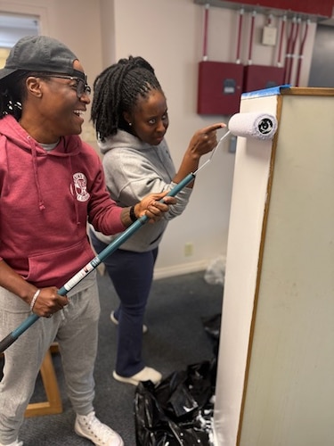 two first sergeants in civilian clothing paint the side of a bookcase white