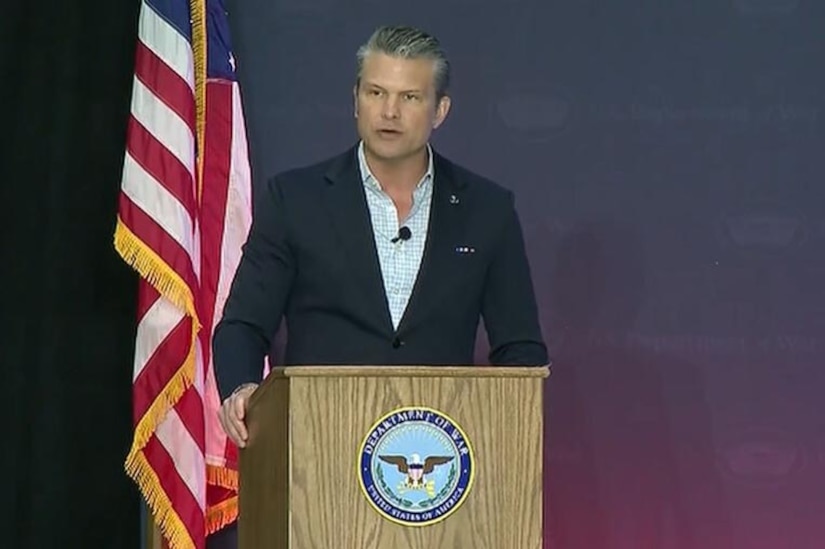 A man in a business suit is speaking from behind a podium with an American flag behind him.