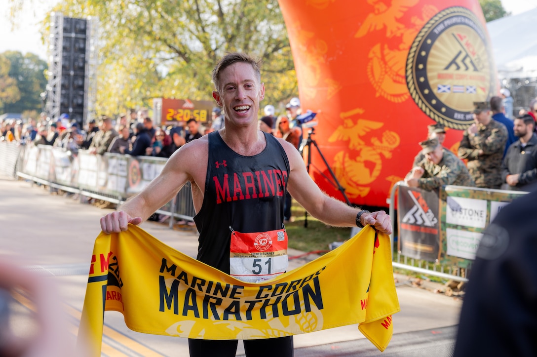 U.S. Marine Corps Maj. Kyle King, the first-place male finisher of the 50th annual Marine Corps Marathon, poses with the Marine Corps Marathon banner in Arlington, Virginia, Oct. 26, 2025. The 2025 “People’s Marathon” featured the hallmark esprit de corps, perseverance, and community spirit the race is known for. Tens of thousands of runners converged on D.C., Maryland, and Virginia to not only show support for the Marine Corps and their country, but also for the unique experience of running this iconic course alongside Marines. (U.S. Marine Corps photo by Sgt. Chancellor Reynolds)