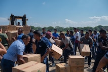 A crown of civilians organize carboard boxes around a large forklift.