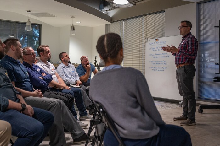 a speaker stands while talking to a group seated in chairs