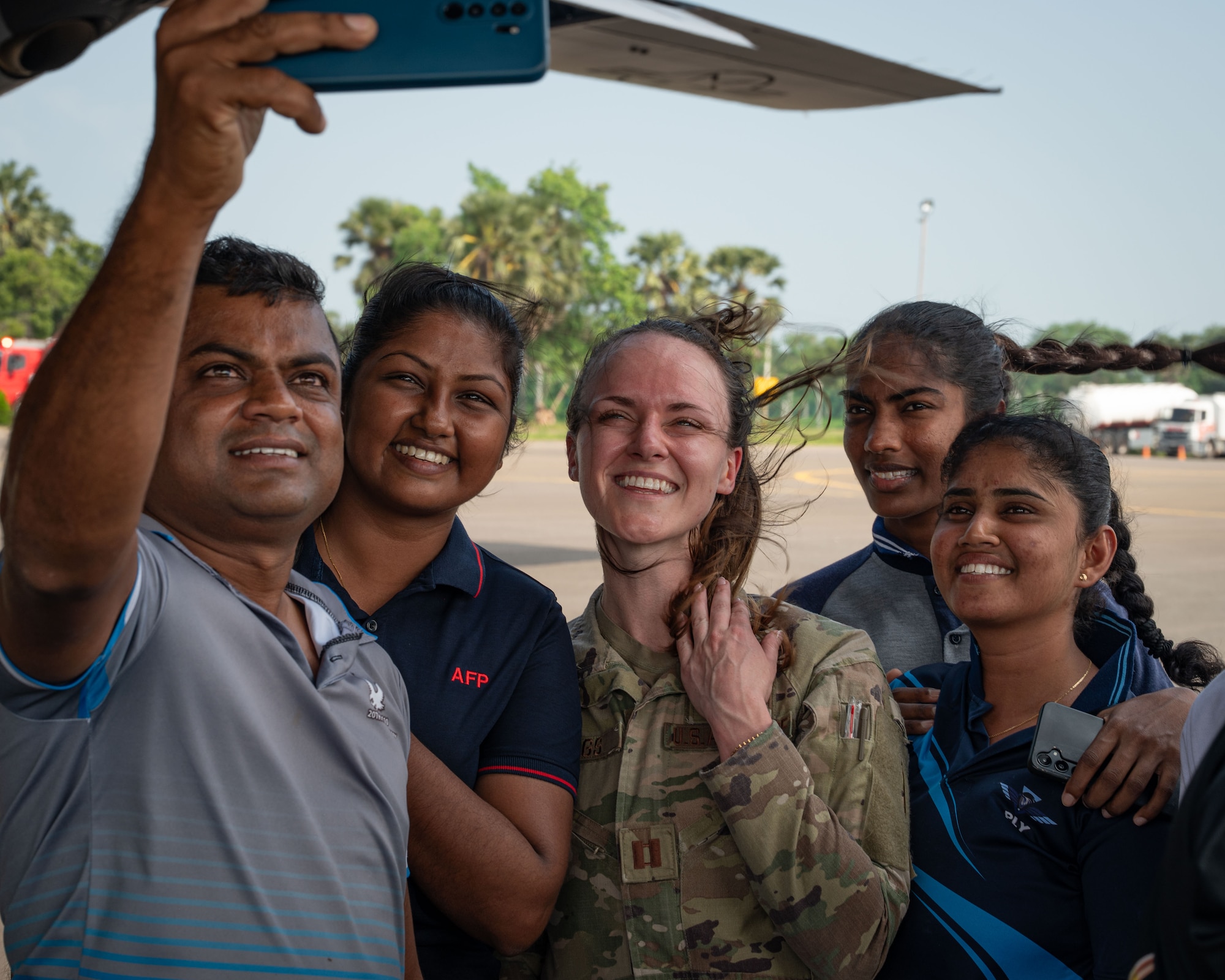 Four civilians crowd around a uniformed female soldier for a selfie.