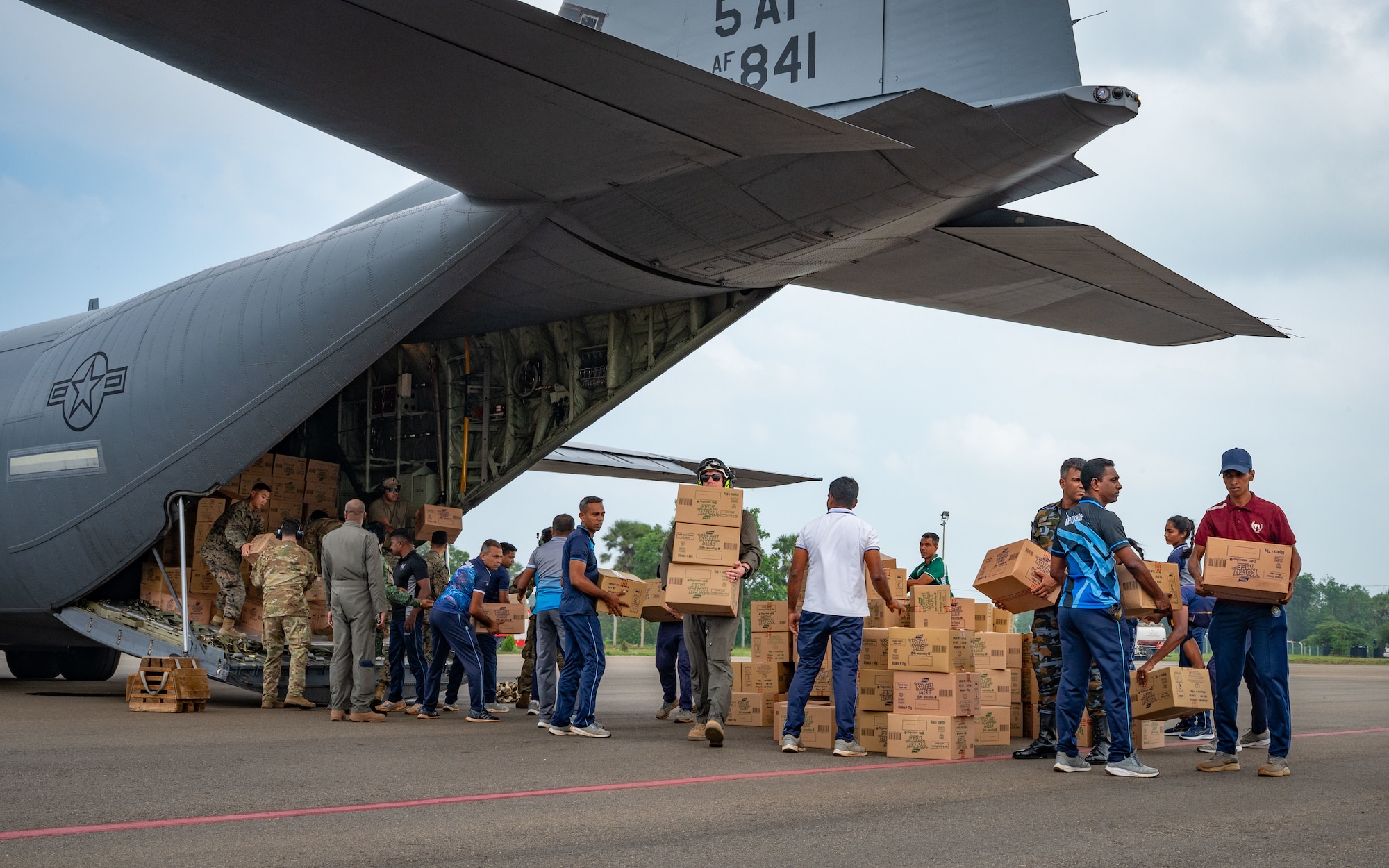 Civilians line up to unload boxes for the rear hatch of a military cargo plane.