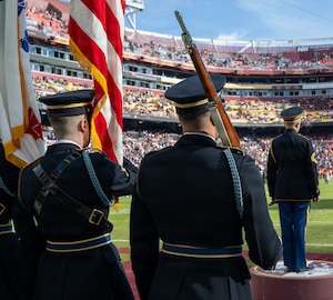 Service members bear the flags during a football game.