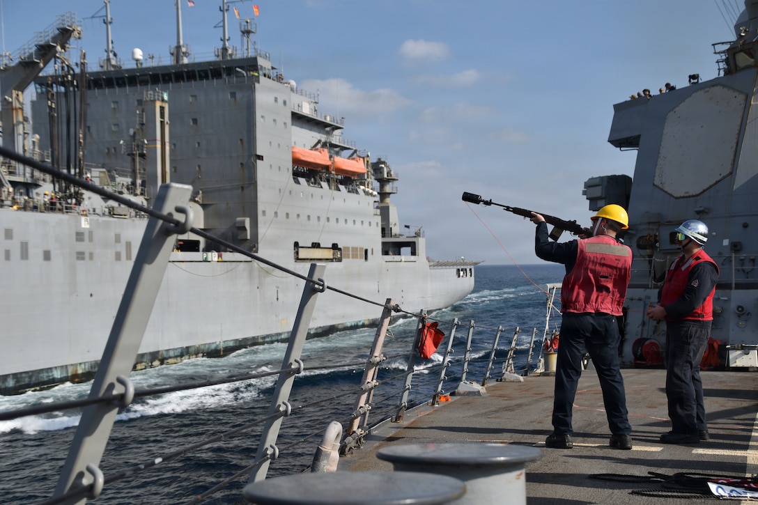 U.S. CENTRAL COMMAND AREA OF RESPONSIBILITY (Jan. 3, 2026) U.S. Navy Fire Controlman 2nd Class Jackson Campbell and Gunner’s Mate 3rd Class Joe Florio, assigned to the Arleigh Burke-class guided-missile destroyer USS McFaul (DDG 74), fire a shot line during a replenishment-at-sea with the Lewis and Clark-class dry cargo ship USNS Carl Brashear (T-AKE-7). McFaul is deployed to the U.S. 5th Fleet area of operations to support maritime security and stability in the U.S. Central Command area of responsibility. (U.S. Navy photo by Chief Intelligence Specialist Aubree Miller)