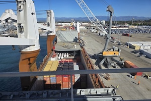 A crane loads cargo containers onto a large docked ship.