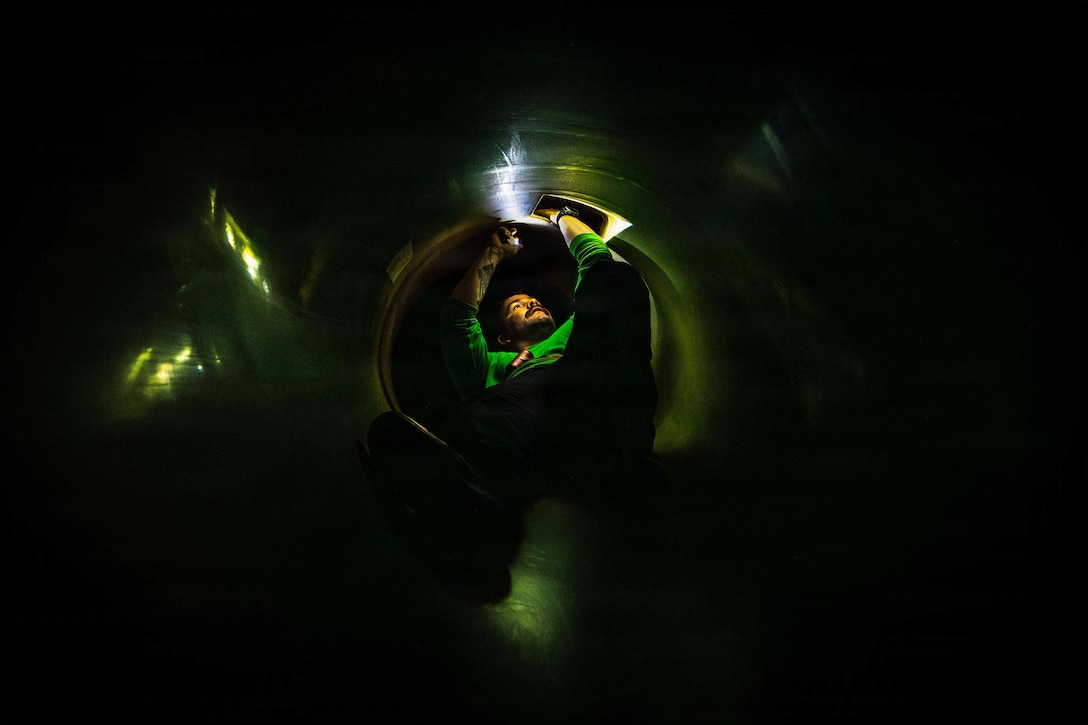 A sailor uses a flashlight to inspect an aircraft in the dark.