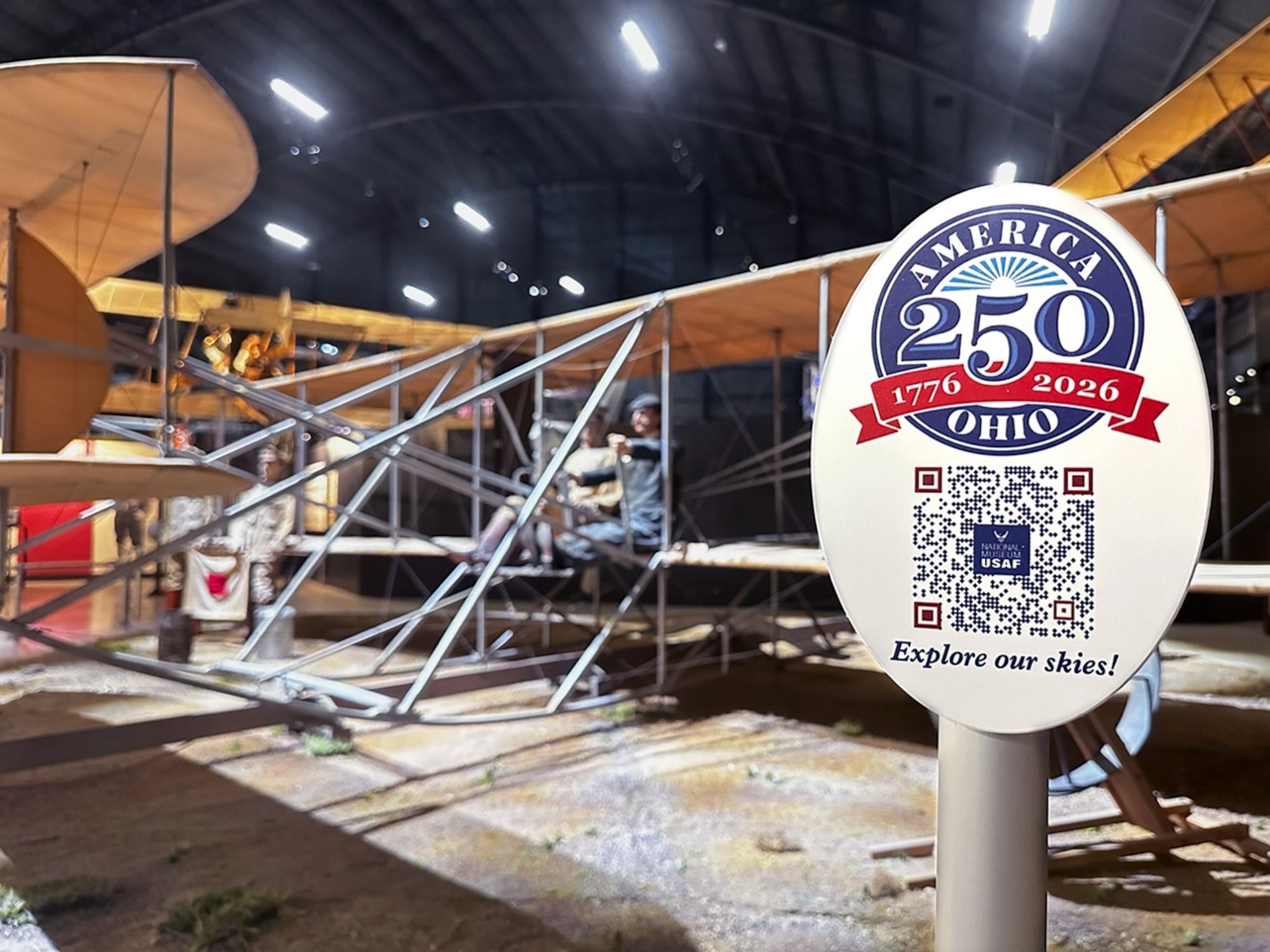 Reproduction of the 1909 Wright Military Flyer next to an America 250-Ohio placard with a QR code inside the National Museum of the U.S. Air Force.