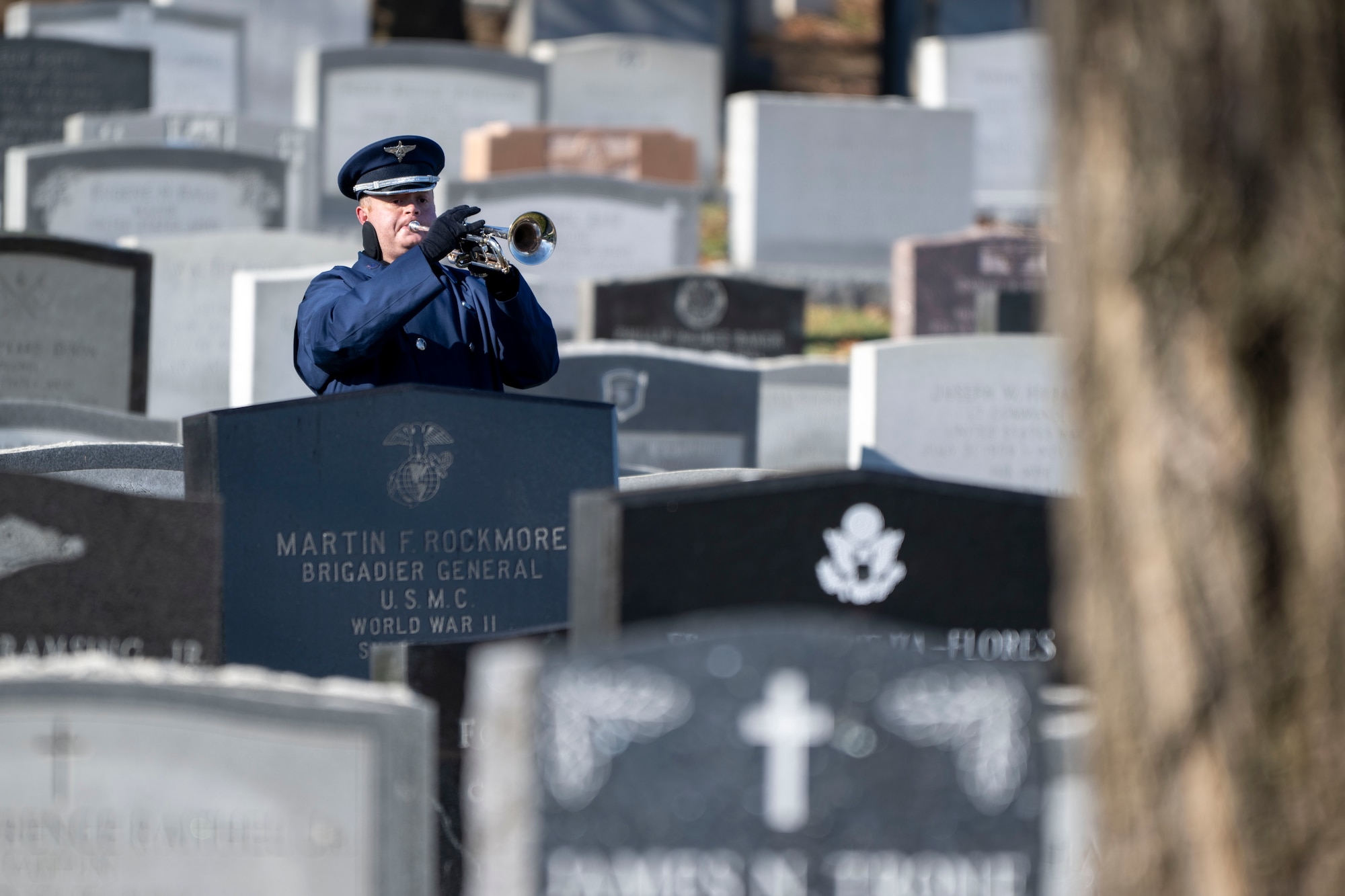 Trumpeter performs in the cemetery surrounded by tombstones.