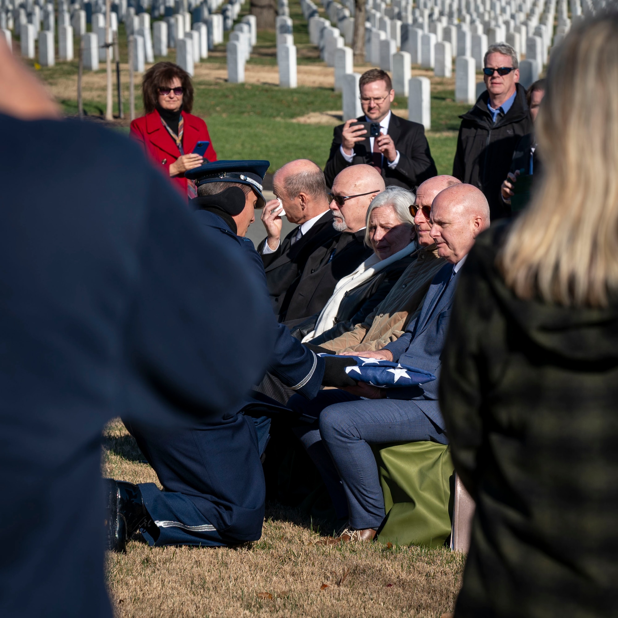 Family sits at a funeral outside while the chaplain hands the flag to the next of kin.