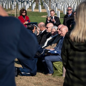 Family sits at a funeral outside while the chaplain hands the flag to the next of kin.