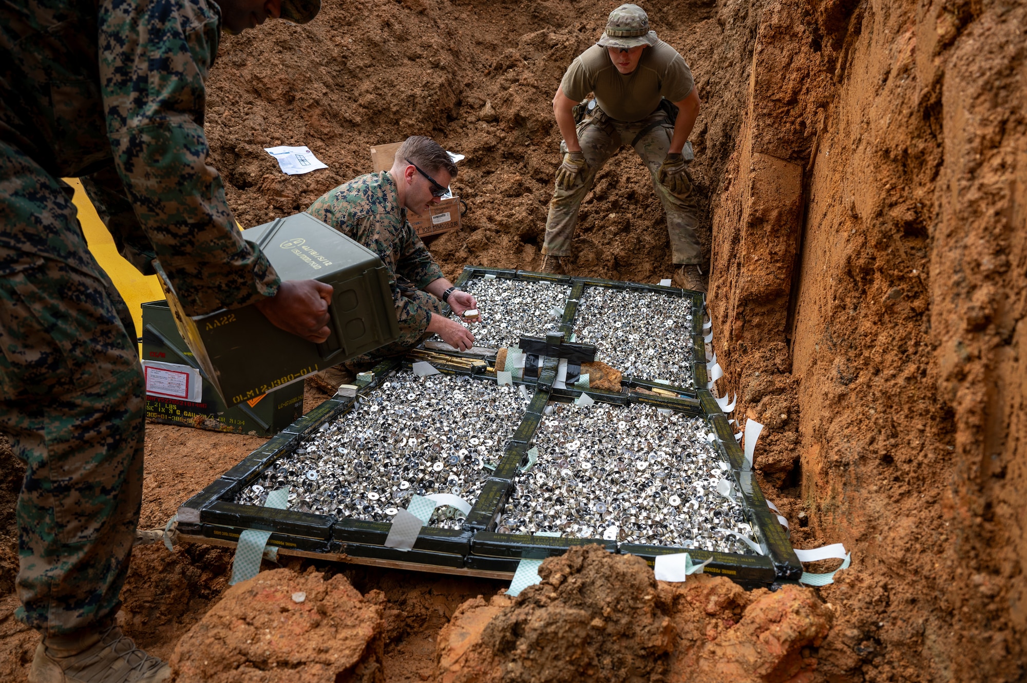 U.S. Air Force Senior Airman Jack Sanderson, center, 18th Civil Engineer Squadron explosive ordnance disposal team member, and U.S. Marines from the 3D Intelligence Battalion prepare unusable Code H munitions for a controlled detonation at Kadena Air Base, Japan, Dec. 18, 2025. Hands-on controlled detonations ensure EOD technicians remain proficient in skills essential to wartime and emergency response missions. (U.S. Air Force photo by Airman 1st Class Francisco Huerta)