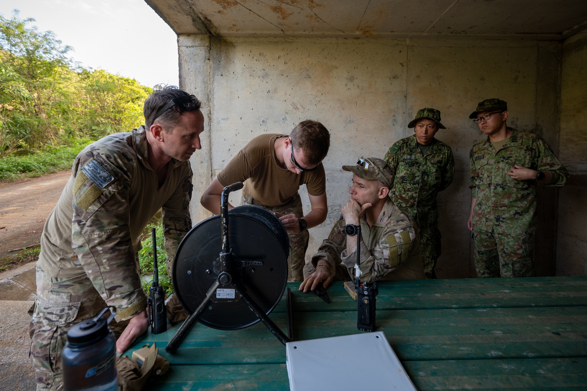 U.S. Air Force 18th Civil Engineer Squadron explosive ordnance disposal members conduct a final safety check of the firing device before a controlled detonation as members from the Japan Ground Self-Defense Force 101st EOD unit spectate at Kadena Air Base, Japan, Dec. 18, 2025. The operation safely eliminated unusable and recovered munitions while reinforcing unit readiness. (U.S. Air Force photo by Airman 1st Class Francisco Huerta)
