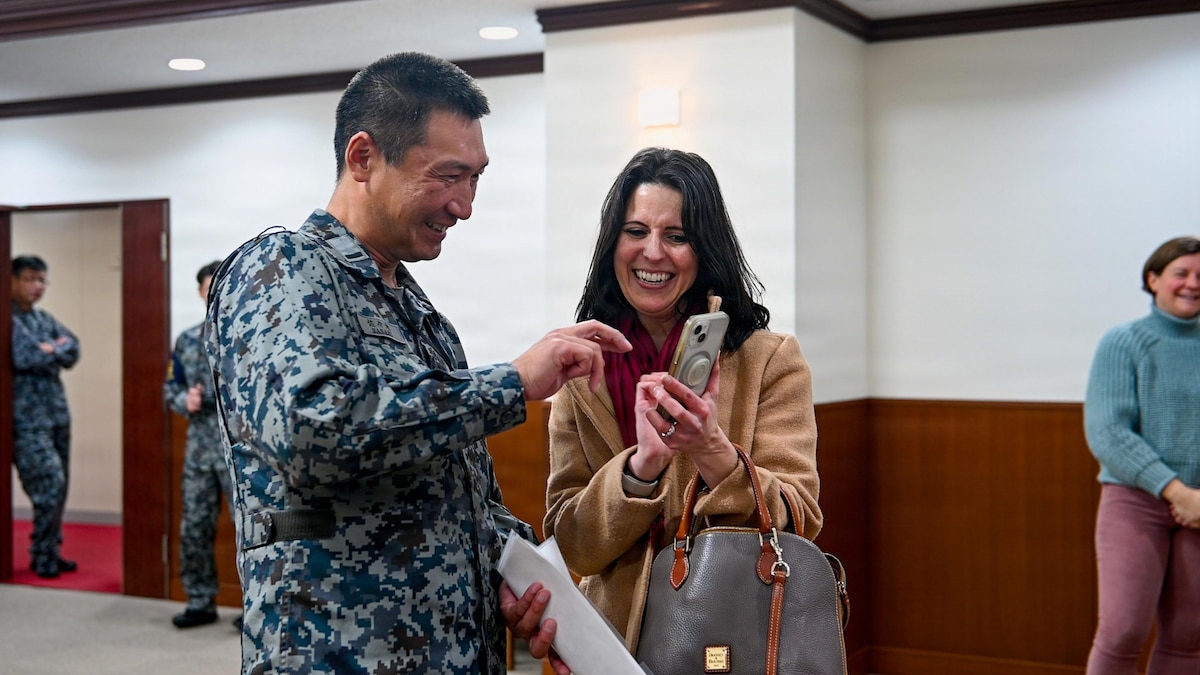 A Misawa Cookie Caper volunteer shows a photo to a Japan Air Self-Defense Force (JASDF) Airman assigned to the 3rd Air Wing at Misawa Air Base, Japan, Dec. 15, 2025. Volunteers delivered homemade cookies to JASDF Airmen a week earlier, with the return gift reinforcing the mutual respect and community bonds that strengthen both bilateral partners. (U.S. Air Force photo by Airman 1st Class Hannah Bench)