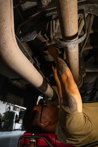 A technician laying down under a bus reaching up into an assembly of equipment.