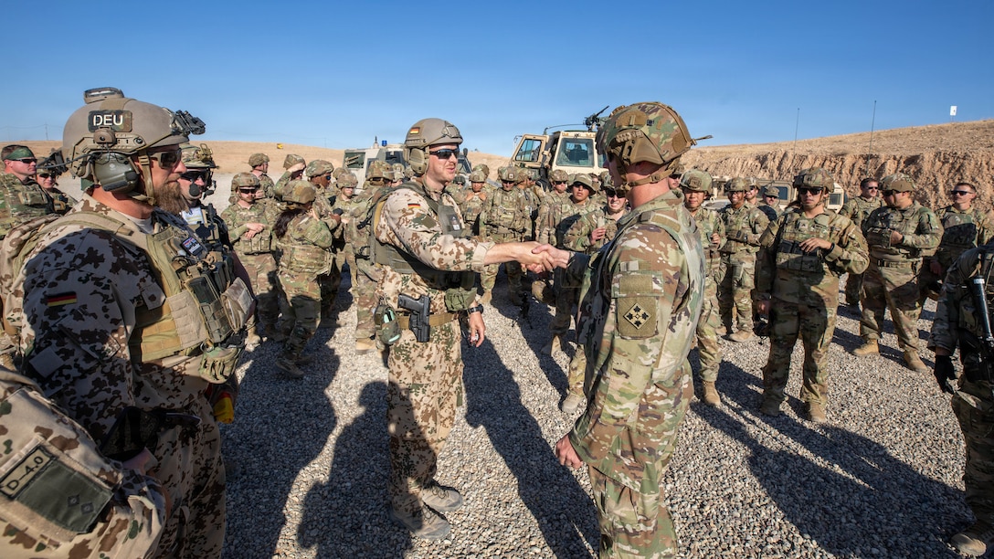 Command Sgt. Maj. Jason Frazee, command sergeant major of 6-17 Cavalry Squadron, 4th Combat Aviation Brigade, 4th Infantry Division, presents a coin and shakes hands with a German Soldier at the conclusion of the Schützenschnur qualification at Beneswala Range on Oct. 31, 2025. The recognition highlighted excellence in multinational marksmanship and reinforced professional bonds between partnered forces. (U.S. Army photo by Spc. Doniel Kennedy.)