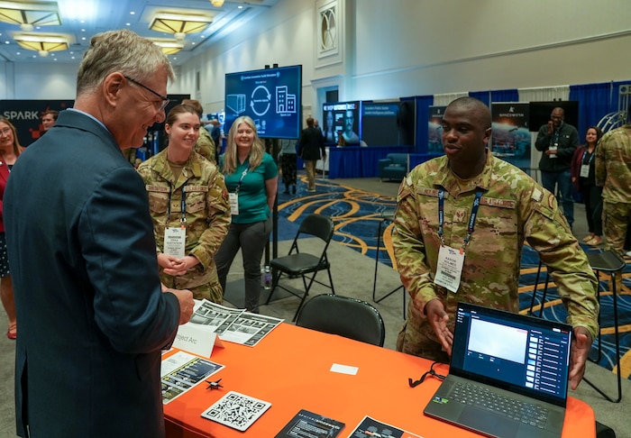 Staff Sgt. Aaron Holmes, AFWERX Spark, briefs Dr. Troy Meink, Secretary of the Air Force, during the Air, Space and Cyber Conference at the Gaylord National Resort and Convention Center in National Harbor, Maryland, on Sept. 24, 2025.