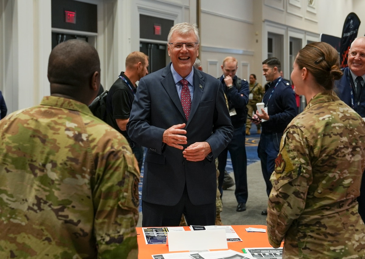 Dr. Troy Meink, Secretary of the Air Force, gets briefed by Staff Sgt. Aaron Holmes and Senior Airman Erika Gustafson, AFWERX Spark, during the Air, Space and Cyber Conference at the Gaylord National Resort and Convention Center in National Harbor, Maryland, on Sept. 24, 2025.