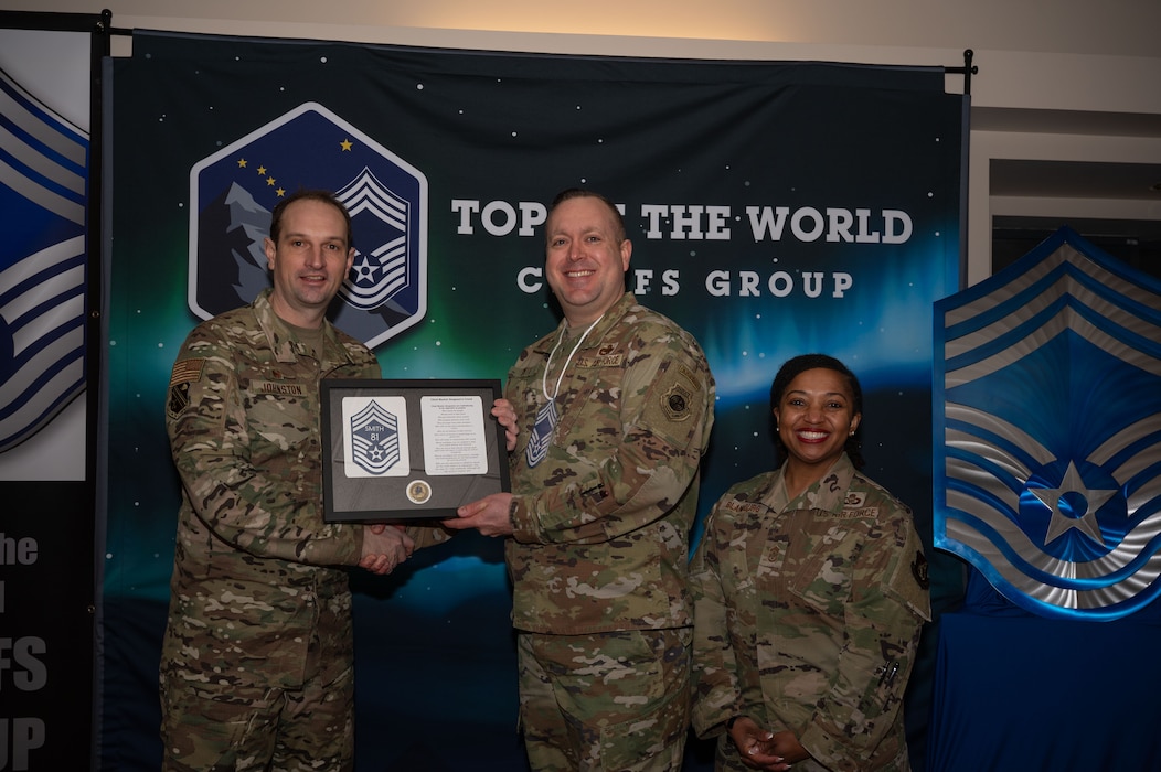 U.S. Air Force Col. Matthew Johnston, 354th Fighter Wing, commander, left, and Chief Master Sgt. Cheronica Blandburg, 354th FW command chief, right, present a certificate to Senior Master Sgt. Adam Smith, 353rd Combat Training Squadron senior enlisted leader, upon his selection to chief master sergeant at Eielson Air Force Base, Alaska, Jan. 6, 2026.