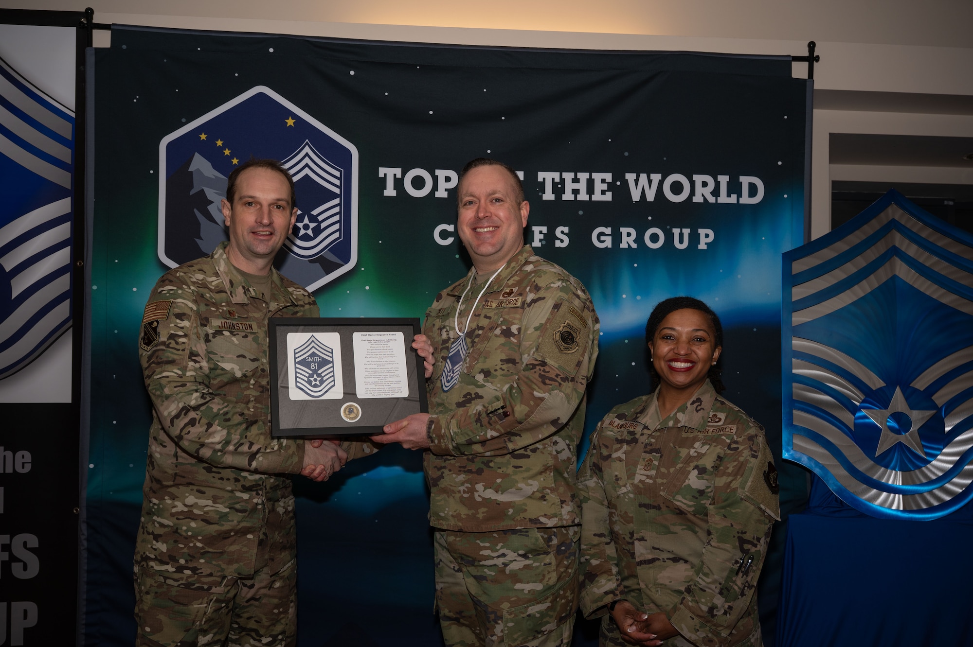 U.S. Air Force Col. Matthew Johnston, 354th Fighter Wing, commander, left, and Chief Master Sgt. Cheronica Blandburg, 354th FW command chief, right, present a certificate to Senior Master Sgt. Adam Smith, 353rd Combat Training Squadron senior enlisted leader, upon his selection to chief master sergeant at Eielson Air Force Base, Alaska, Jan. 6, 2026.