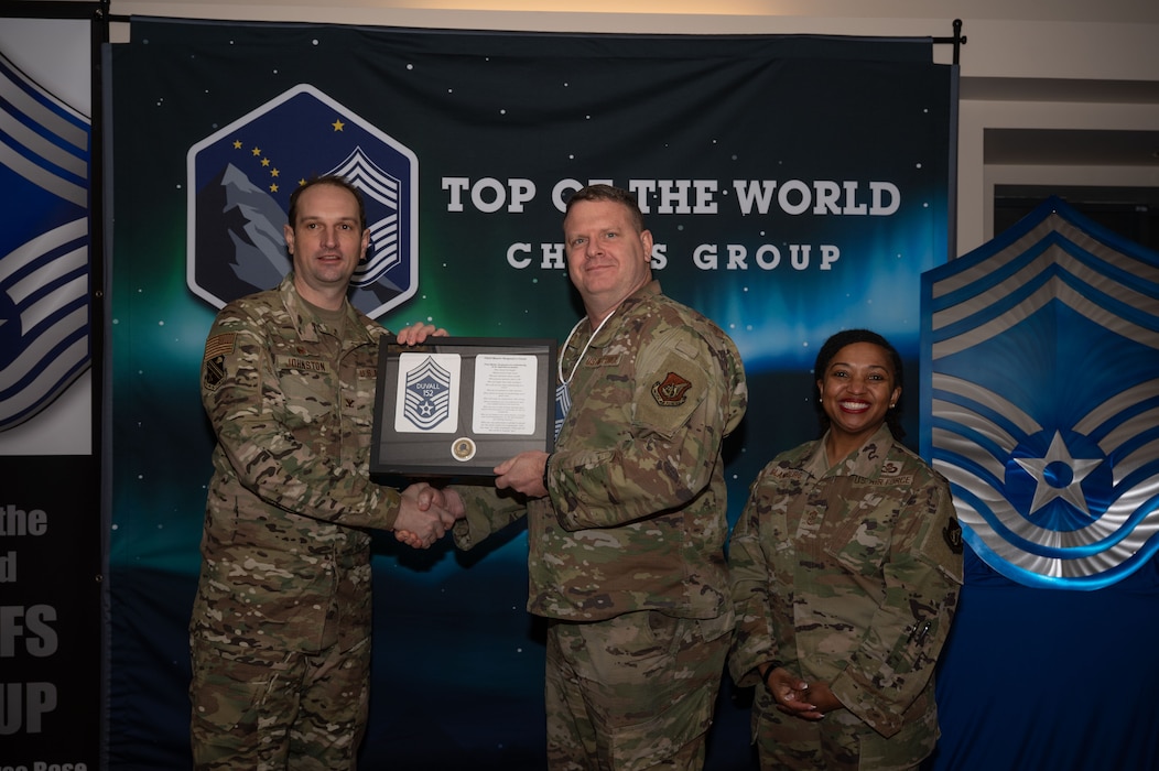 U.S. Air Force Col. Matthew Johnston, 354th Fighter Wing commander, left, and Chief Master Sgt. Cheronica Blandburg, 354th FW command chief, right, present a certificate to Senior Master Sgt. Scott Duvall, 354th Maintenance Squadron superintendent, upon his selection to chief master sergeant at Eielson Air Force Base, Alaska, Jan. 6, 2026.