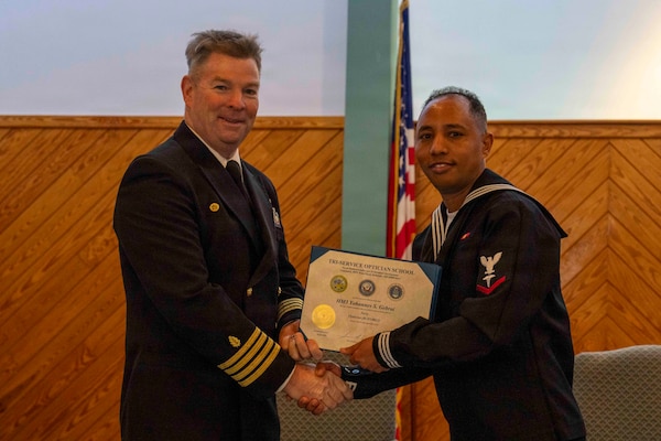 251216-N-JC800-1022 YORKTOWN, Virginia (Dec. 16, 2025) - Capt. James Corbett, commanding officer of Naval Medical Leader and Professional Development Command, presents a certificate of completion to Hospital Corpsman 3rd Class Yohannes Gebrai during the graduation ceremony for the Tri-Service Optician School Class 25010, Dec. 16. (U.S. Navy photo by Mass Communication Specialist 1st Class Heath Zeigler/Released)