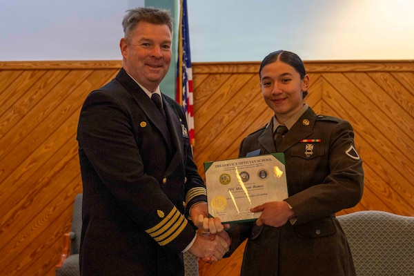 251216-N-JC800-1022 YORKTOWN, Virginia (Dec. 16, 2025) - Capt. James Corbett, commanding officer of Naval Medical Leader and Professional Development Command, presents a certificate of completion to U.S. Army Pfc. Monseratt Ramos during the graduation ceremony for the Tri-Service Optician School Class 25010, Dec. 16. (U.S. Navy photo by Mass Communication Specialist 1st Class Heath Zeigler/Released)