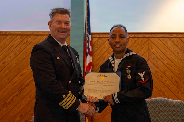 251216-N-JC800-1022 YORKTOWN, Virginia (Dec. 16, 2025) - Capt. James Corbett, commanding officer of Naval Medical Leader and Professional Development Command, presents a Navy and Marine Corps Achievement Medal to Hospital Corpsman 3rd Class Yohannes Gebrai during the graduation ceremony for the Tri-Service Optician School Class 25010, Dec. 16. (U.S. Navy photo by Mass Communication Specialist 1st Class Heath Zeigler/Released)