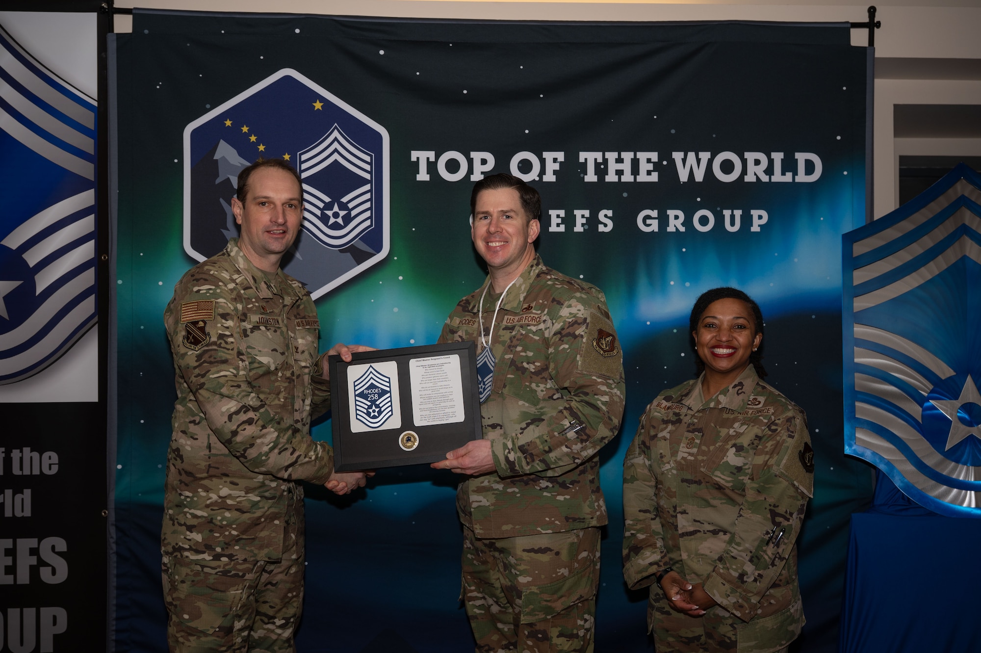 U.S. Air Force Col. Matthew Johnston, 354th Fighter Wing commander left, and Chief Master Sgt. Cheronica Blandburg, 354th FW command chief, right, present a certificate to Senior Master Sgt. Brandon Rhodes, 354th Maintenance Group F-35 lead production superintendent, upon his selection to chief master sergeant at Eielson Air Force Base, Alaska, Jan. 6, 2026.