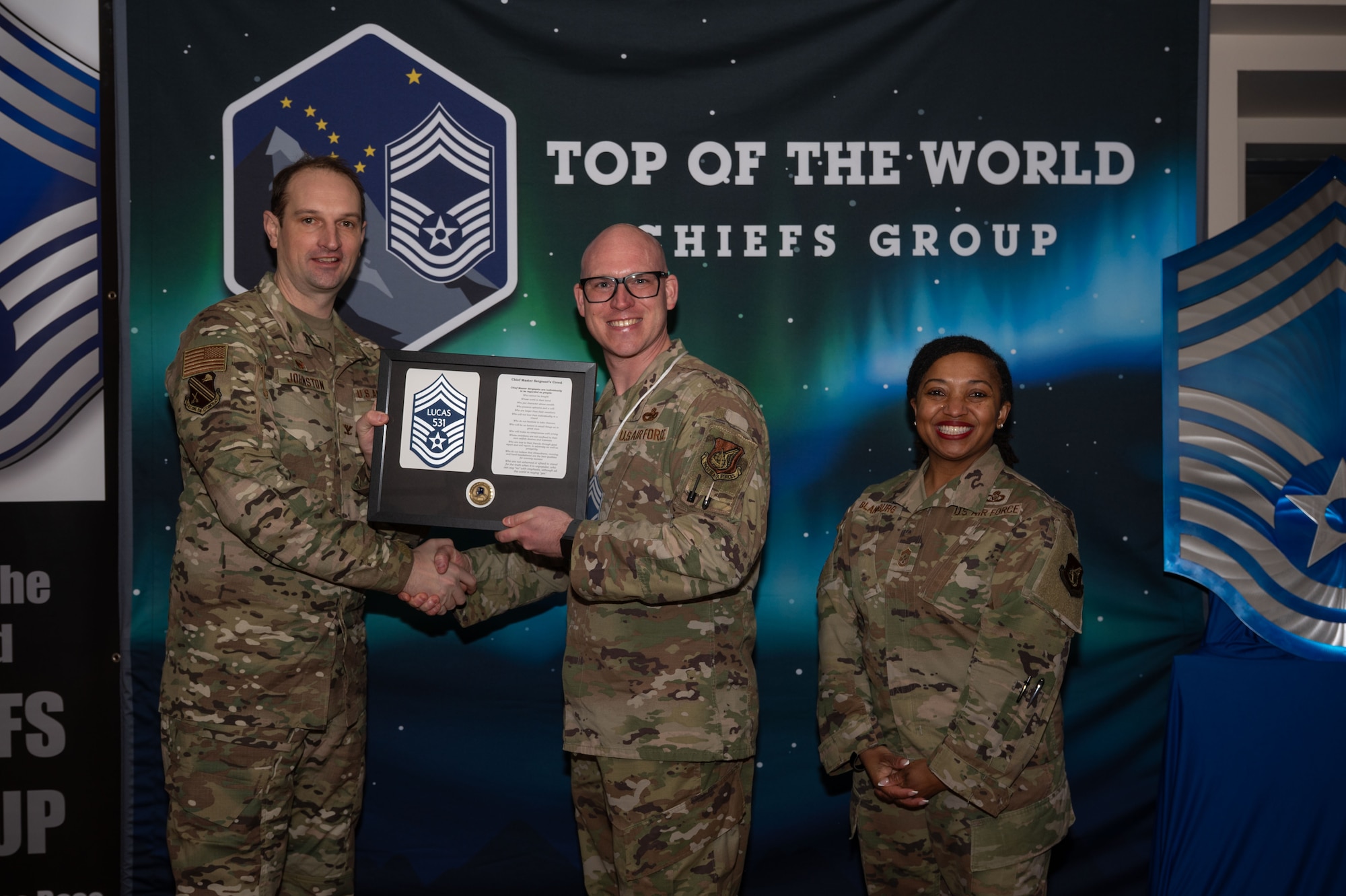U.S. Air Force Col. Matthew Johnston, 354th Fighter Wing commander, left, and Chief Master Sgt. Cheronica Blandburg, command chief, right, present a certificate to Senior Master Sgt. Michael Lucas, 354th Logistics Readiness Squadron superintendent, upon his selection to chief master sergeant at Eielson Air Force Base, Alaska, Jan. 6, 2026.