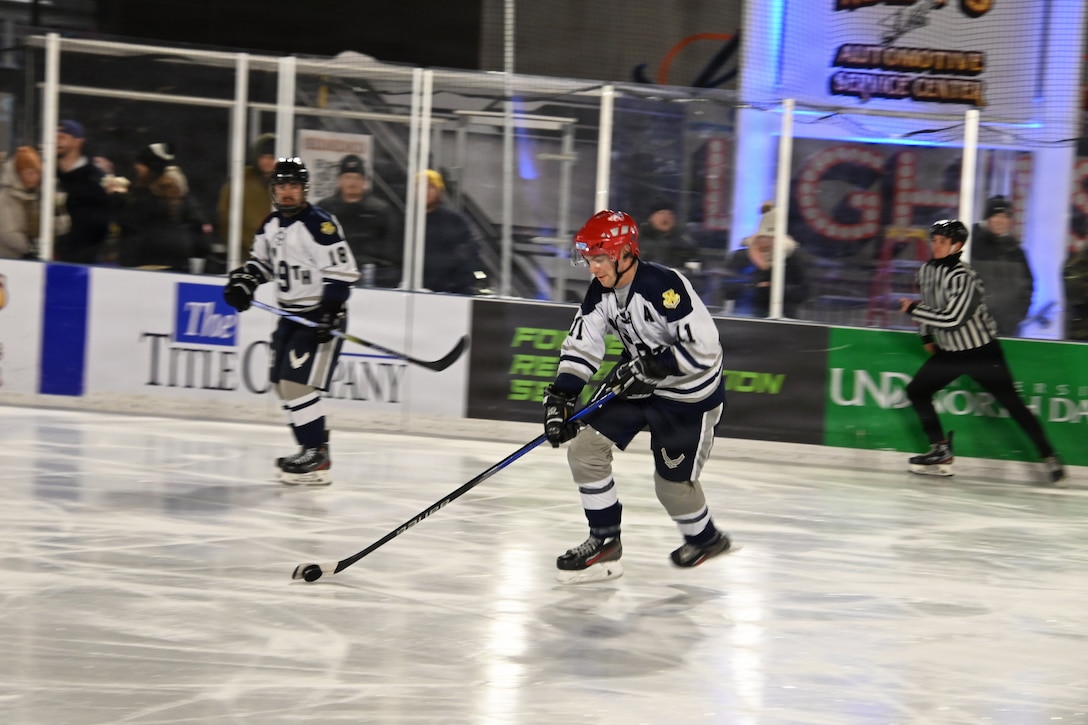 An airman in hockey gear handles a puck while skating on the ice during a game.