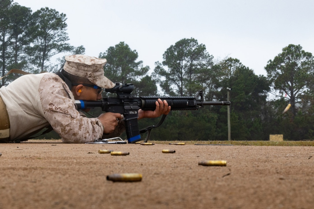 A Marine lying on the ground fires a weapon as ammo sits on the ground.