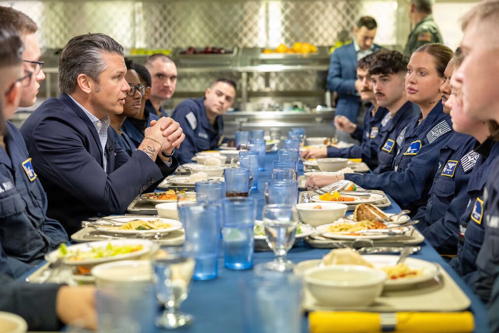 The secretary of war eats lunch with sailors in a cafeteria.
