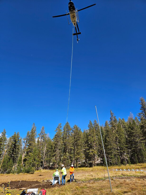 Helicopter with long rope hanging down to pick up rocks.
