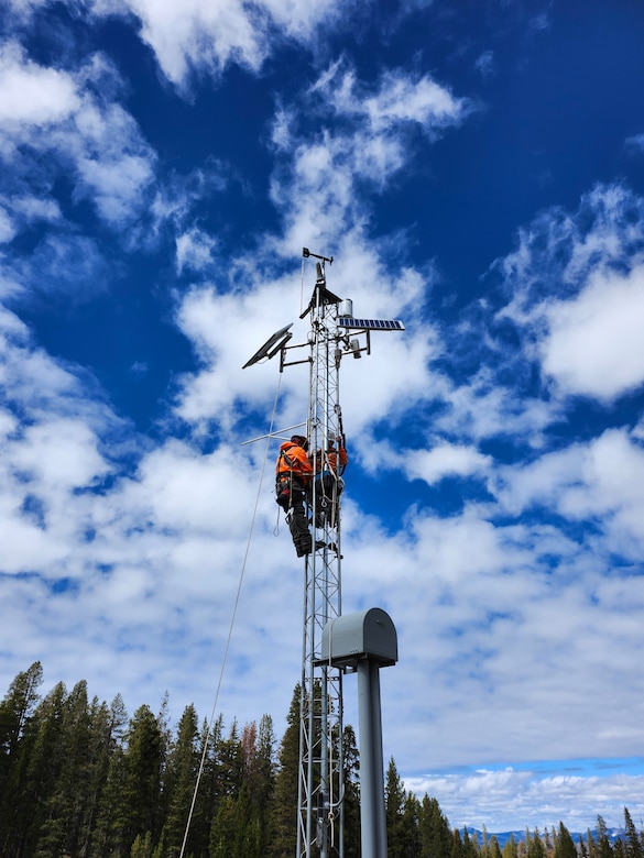 Workers climbing on weather station tower.