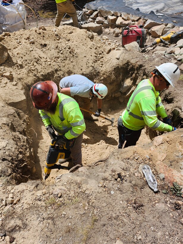 Three men digging in ditch.